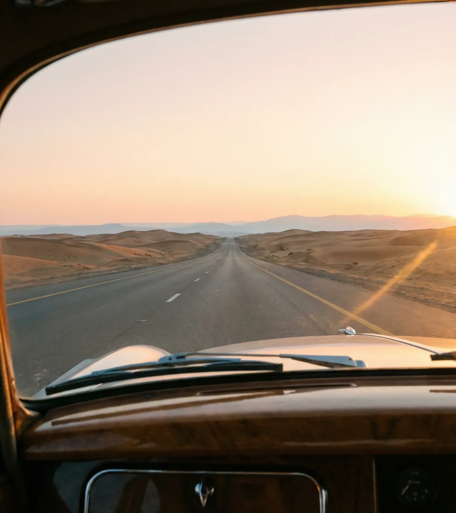 A long desert road reaching toward the Hajar mountains at dusk