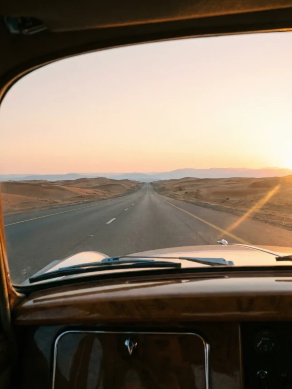 A long desert road reaching toward the Hajar mountains at dusk